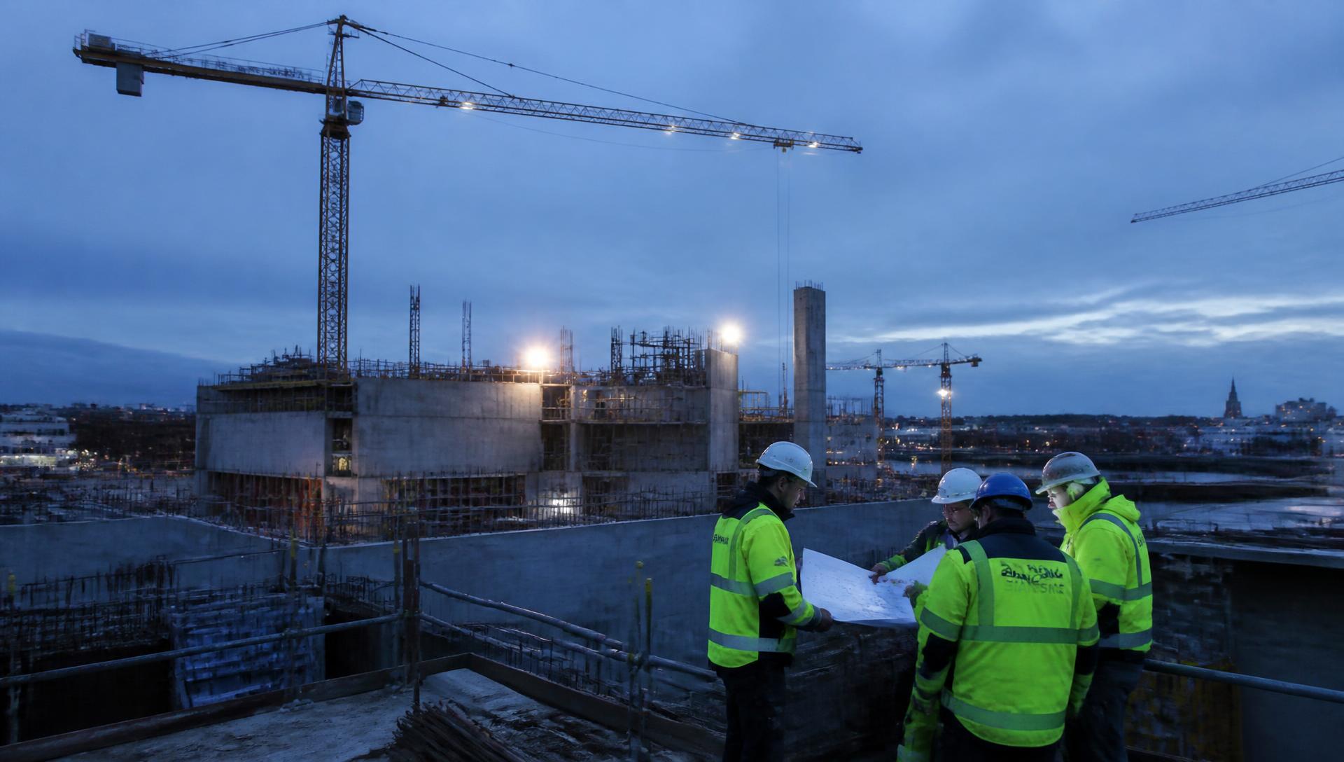 Byggarbetsplats i skymning med kranar och projektledare som granskar ritningar